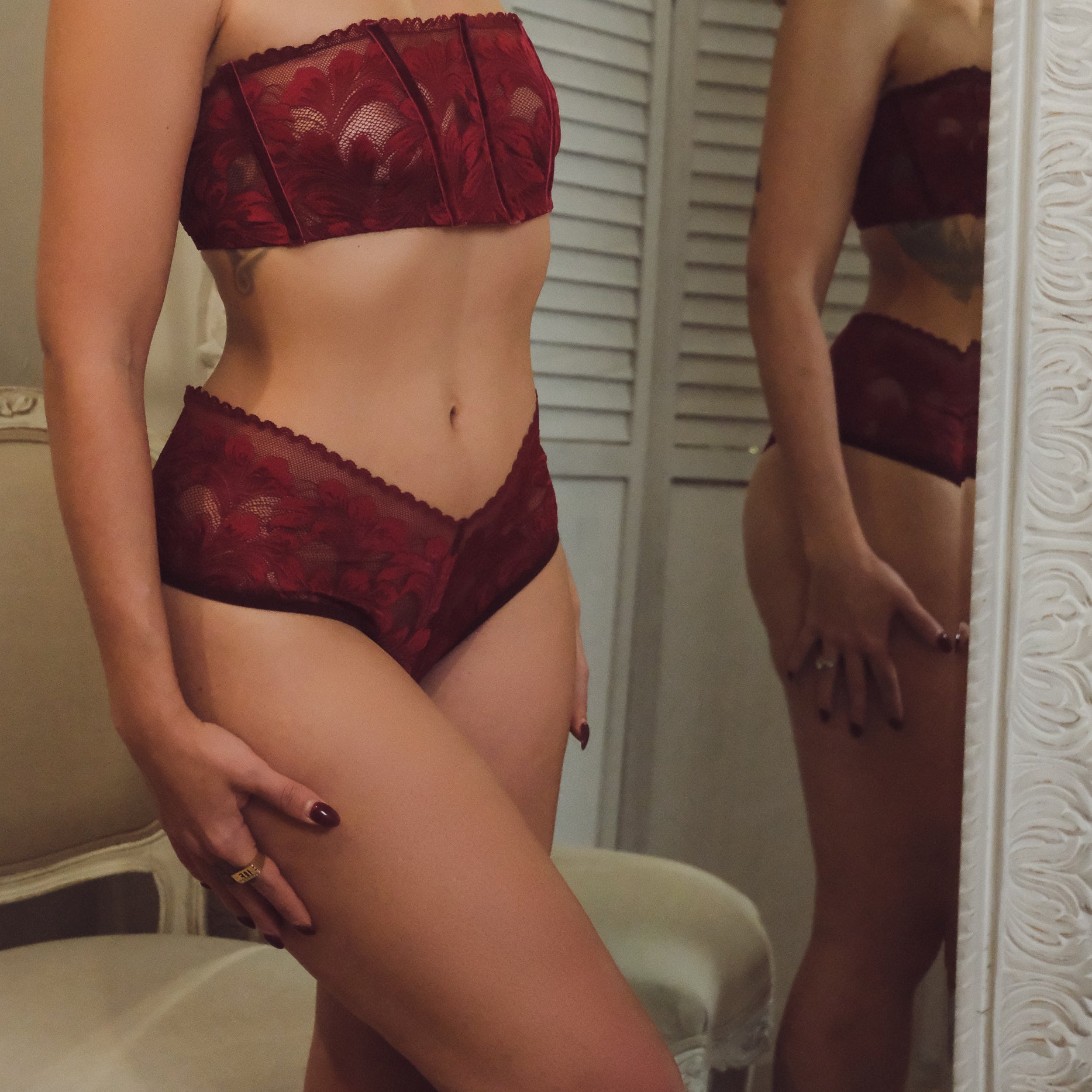 Woman wearing red lace lingerie standing in front of a mirror.