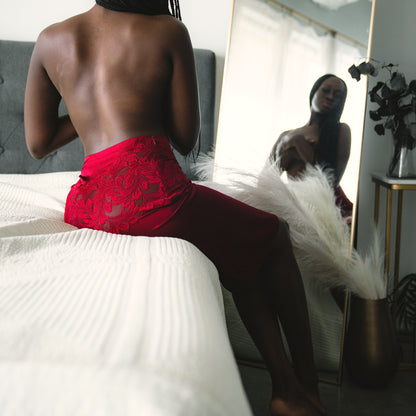 Woman wearing red lace skirt sitting on a bed in front of a mirror.