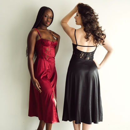 Two women wearing red and black satin slip dresses against a plain background